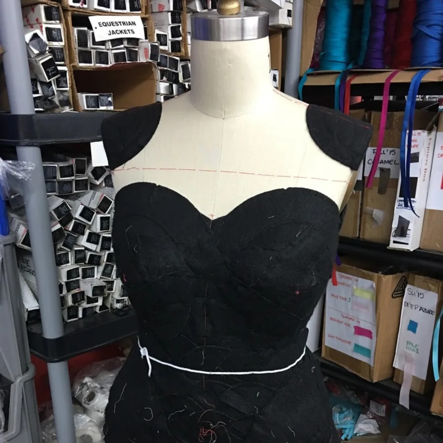 Black garment being draped and fitted on a dress form in a garment workroom