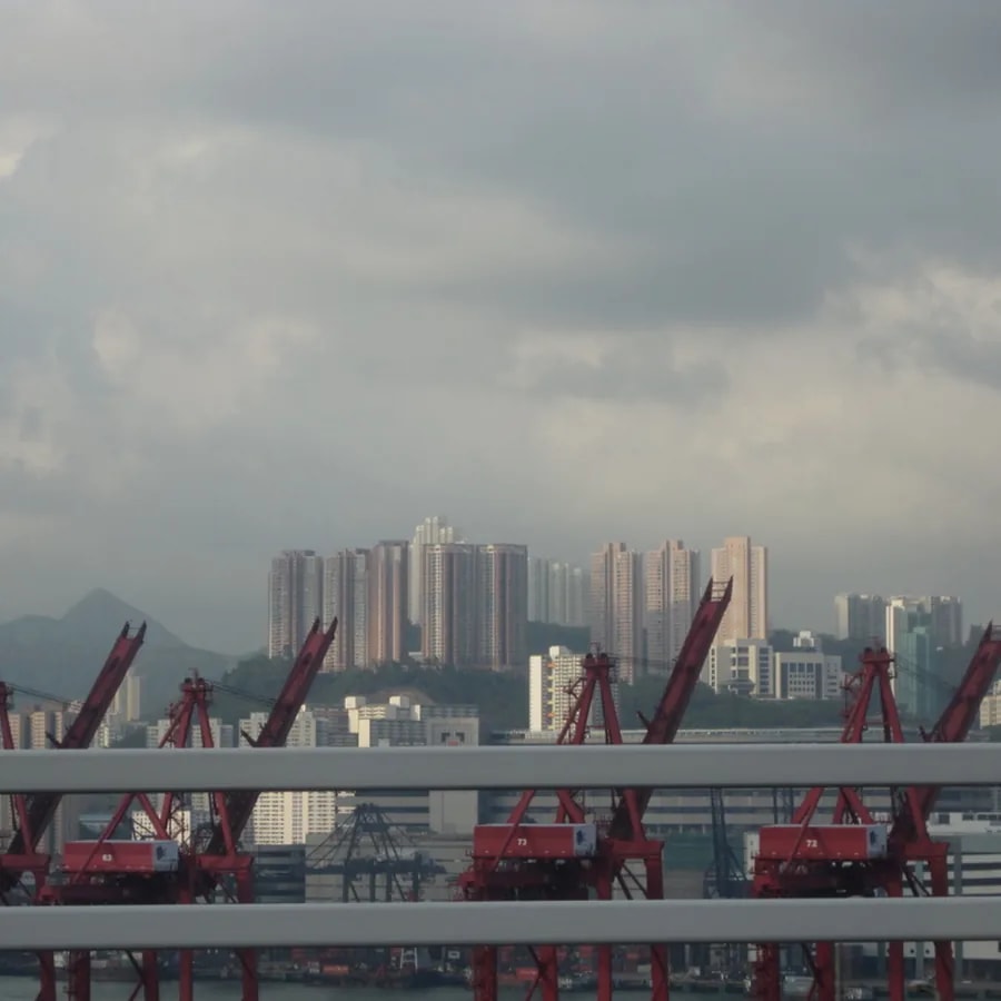 Hong Kong harbor with cargo cranes and apartment towers beneath a cloudy sky