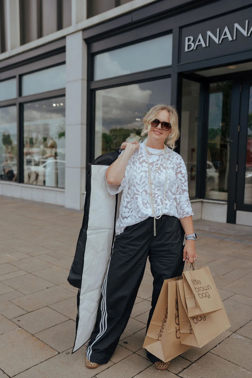 Monika in a casual outfit with a white lace top, black wide-leg pants, and leopard print sneakers